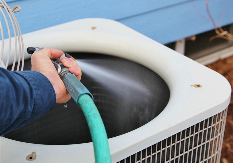Technician cleaning an outdoor A/C condenser coil